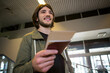 © Wavebreak Media - Male traveler wearing green jacket standing at airport concourse holding passport and boarding pass