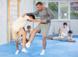 © JackF - Concentrated experienced trainer showing basic self-defense techniques to group of motivated teens at training center, performing foot sweep during simulated sparring with boy