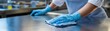© AGI Studio - A person wearing blue gloves is cleaning a stainless steel surface with a blue cloth in a professional kitchen or industrial setting.