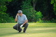 © Montri - Senior golfer crouching on green grass, focusing on golf ball alignment before putting. Concept of concentration, strategy, and active lifestyle for older adults in outdoor sports.