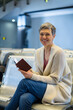 © Wavebreak Media - Mature woman holding open passport sitting on bench by flight display in airport lounge, copy space
