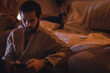© Wavebreak Media - Bearded man mid-30s sitting on floor leaning on sofa cushion and checking smartphone under lamp