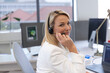 © Wavebreak Media - Woman wearing headset and blazer turning toward camera while working on laptop at desk with monitor