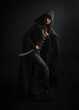 © faestock - portrait of mysterious hooded woman in black cloak, gothic fantasy or dystopian character, holding sword weapon. lit with moody cinematic shadows, studio scene on dark isolated background