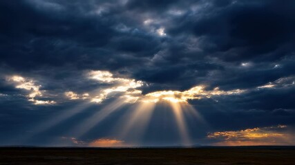 Wall Mural - golden light beams pierce through an opening in dark clouds, illuminating a vast landscape at sunset
