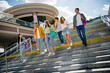© deagreez - Cheerful young students walking together outdoors under a bright summer sky near modern architecture.