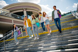 Cheerful young students walking together outdoors under a bright summer sky near modern architecture.