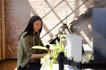 Asian woman coding on laptop in modern office, smiling and focused