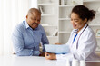 © Anastasiya - Happy African American doctor reviewing medical records with smiling black mature male patient during visit in modern clinic, therapist woman discussing test results with man, closeup