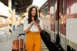 © Home-stock - Positive young lady traveler using her smartphone while standing at train platform. People and transportation concept