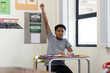 © Wavebreak Media - Multiracial child boy student raising hand at metal desk in school classroom, using open notebook
