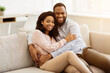 © Prostock-studio - Happy Loving Family. Beautiful african american man and woman cuddling and relaxing on the couch at home in living room, smiling couple looking at camera and posing, spending leisure time together