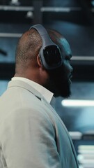 Poster - Vertical video Happy manager listening music, walking in data center with blinking lights on rigs showing system activity. Cheerful man wearing headphones overseeing dimly lit server farm, camera B