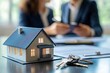 © Tyo - Miniature house model sits on desk;  business people in the background