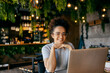 © Dusan Petkovic - Portrait of happy interracial female remote worker sitting in cafe and smiling at camera.