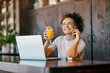 © Dusan Petkovic - Portrait of interracial remote worker sitting in cafe with orange juice in hands and talking on cellphone.