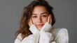 © fotofabrika - Woman in cozy sweater smiles warmly with hands on her face in a minimalist indoor setting during daylight