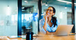 © (JLco) Julia Amaral - Smiling woman wearing glasses working at a desk with a laptop