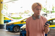 © Ranta Images - Young Asian gay teen tourist using phone outdoors with taxis behind