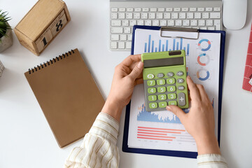 Fototapete - Female accountant with calculator, notebook, keyboard and financial graphics at table in office