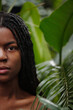 © pressmaster - Vertical portrait of young woman with natural hair peeking through lush green jungle foliage. Close-up capturing serene expression and connection with nature