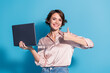 © deagreez - Smiling young woman holding a laptop giving thumbs up with blue background, expressing confidence and success