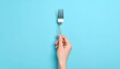 © Abdul - Close up photo of a hand holding a fork against a plain soft blue background
