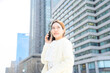 © Yamatatsu - 春の陽射しの中でスマートフォンを耳に当てて微笑む白ジャケットの女性のビジネス風景