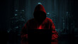 © Curioso.Photography - A mysterious hooded figure sits in front of a laptop, illuminated by a red glow, with a dark, abstract city background.
