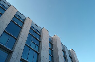Poster - Modern building with large windows against clear blue sky. Architectural design featuring clean lines, geometric shapes. Office windows reflect sky, offering commercial, business themes. Contemporary