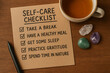 © PixelPlace - self-care routine. A self-care checklist on paper lists five wellness tips next to a cup of tea, crystals, and a pen on a wooden surface.