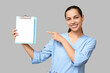 © Pixel-Shot - Portrait of female doctor pointing at clipboard with blank paper sheet on grey background
