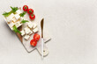 © Pixel-Shot - Fresh feta cheese cubes with rucola and cherry tomatoes on marble cutting board with knife, a golden knife rests beside the ingredients, ready for culinary preparation