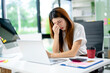 © Nuttapong punna - Frustrated woman holding head in hands at office desk with laptop and smartphone.