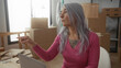 © Krakenimages.com - Senior woman with grey hair works on a laptop in a new apartment, surrounded by moving boxes, indicating a recent move and engagement with technology in a home setting.