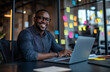 © 44designstore - A young Smiling businessman in a modern office, holding a smartphone, sitting at a desk with a laptop, colorful sticky notes covering a dark blue glass wall behind him, creative and productive