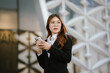 © Witoon - Businesswoman in black suit holding laptop and smartphone smiling confidently outdoors in modern urban environment