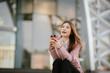 © Witoon - Businesswoman in pink suit holding laptop and smartphone smiling confidently outdoors in modern urban environment