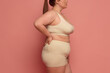 © Lustre Art Group  - A woman confidently embraces her natural body in comfortable beige underwear against a pink background. Concept of body positivity and self-love.