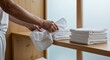 © Zhanna - Person folding white towels on wooden shelf in modern setting
