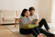 © angutyo - young couple sitting on the floor and using interent on digital tablet concept pareja joven sentada en el suelo y utilizando interent en tableta digital concepto jeune couple assis utilisant
