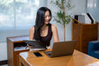 © Apichat - A woman is sitting at a desk with a laptop and a clipboard