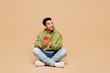 © ViDi Studio - Full body young man of African American ethnicity wears green hoodie casual clothes sit hold in hand use mobile cell phone look aside isolated on plain pastel light beige background Lifestyle concept