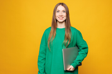 Young smiling Caucasian IT woman she wear green sweatshirt casual clothes hold use closed laptop pc computer look camera isolated on plain yellow orange background studio portrait. Lifestyle concept.
