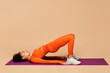 © ViDi Studio - Full body young fitness trainer instructor sporty woman wear orange clothes spend time in gym do glute bridge exercise on yoga mat o isolated on plain beige background. Workout sport fit abs concept.