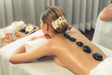 Hot stone massage at spa salon in luxury resort with day light serenity ambient, blissful couple customer enjoying spa basalt stone massage glide over body with soothing warmth. Quiescent