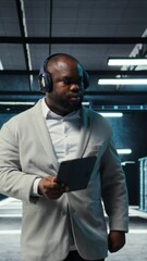 Poster - Vertical video Server room programmer wearing headphones troubleshooting errors using software on tablet. IT specialist listening music, walking in data center fixing bugs using device , camera A