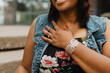 © Jordan - Close-up of a smiling woman wearing a denim vest over a floral dress, hand with red manicure and solitaire engagement ring on her chest beside a silver cuff bracelet