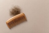 A wooden comb rests beside a clump of brown hair on a beige surface