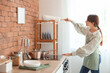 © Pixel-Shot - Pretty young woman with pp-duster cleaning shelf in kitchen